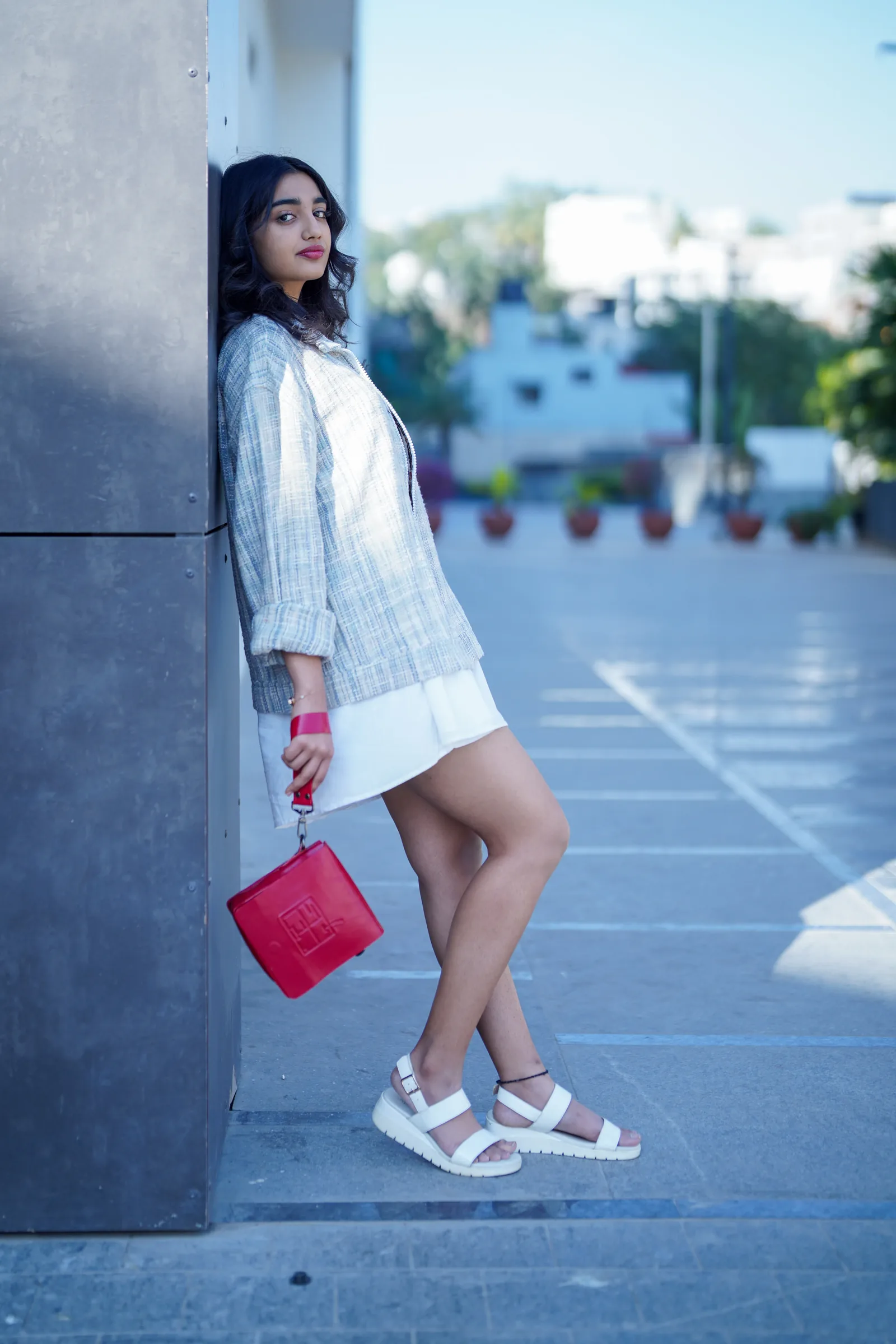 Model leaning against a wall with red bag